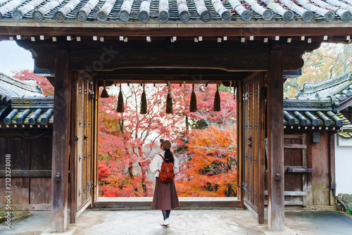 Back view of a female tourist visiting a traditional Japanese temple gate in Kyoto during vibrant autumn season