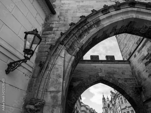 Black and white view of Gothic arches at the Lesser Town Bridge Tower with St. Nicholas Church in the background in Prague, Czechia.