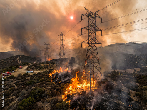 High voltage power lines burning in wildfire. Electrical infrastructure damaged by forest fire.