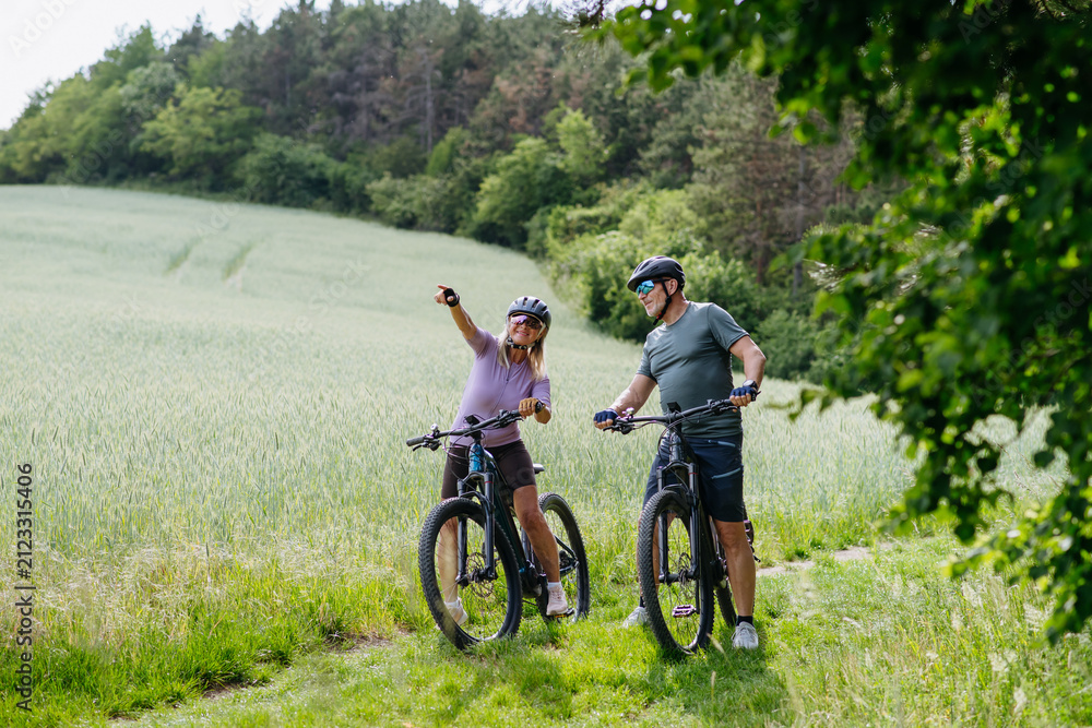 Naklejka premium Senior couple taking break during e-bike ride, enjoying nature around them.