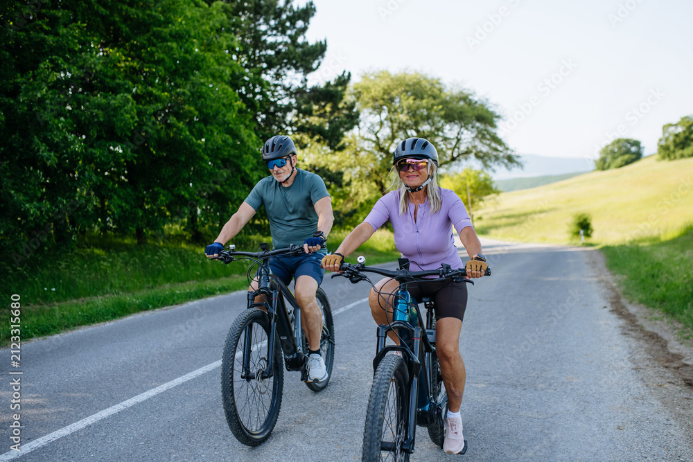 Fototapeta premium Happy mature couple riding e-bikes through scenic countryside.