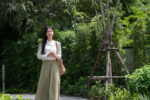 Obraz na plátně Young Asian woman holding coffee cup and enjoying a nature on a peaceful walk in green garden park