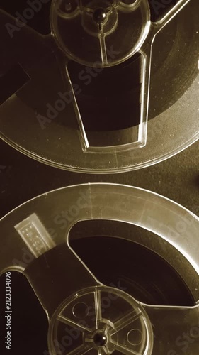 Vertical close up of a reel to reel tape recorder with two transparent spools of magnetic tape rotating. Retro analog audio equipment for vintage sound and archive footage