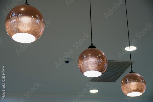 Three modern copper pendant lights hanging from a ceiling with recessed lighting