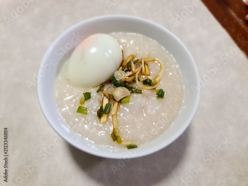 Chinese style minced pork in plain rice porridge topped by hardboiled egg, ginger and green onion for breakfast on gray table