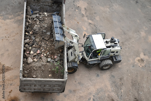 Aerial view of construction site where a front loader is loading soil, rocks, and debris into a dump truck, industrial work, excavation, and earthmoving processes