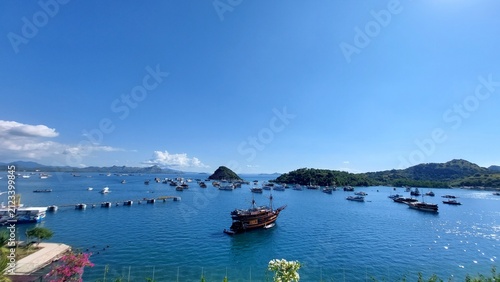 Foto A panoramic, wide-angle shot of a vibrant tropical bay with phinisi boats on the water and lush, green hilly islands under a clear blue sky
