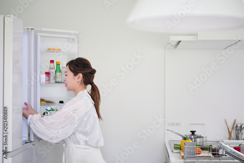 冷蔵庫を開けキッチンで料理を作る女性