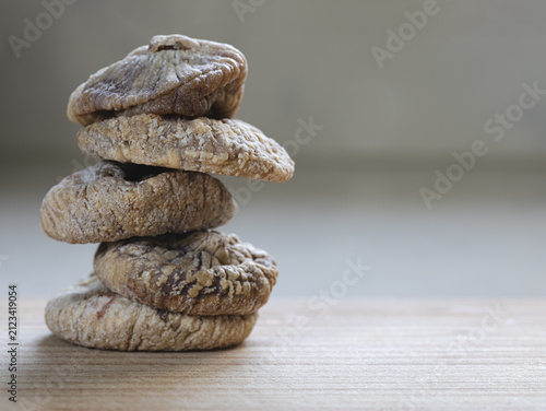 A stack of naturally dried figs on a wooden table, illuminated by soft natural light. Warm earthy tones, rich textures, and generous copy space create a rustic food composition.