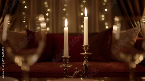 Romantic candlelight setting with blurred wine glasses and bokeh fairy lights creating a cozy luxury atmosphere for a special evening date or celebration.