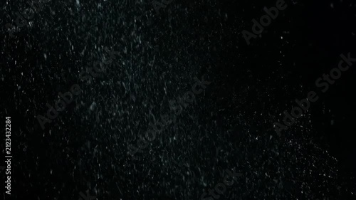Abstract white particles falling slowly like dust, snow or fine rain against a deep black background. Cinematic visual effect overlay footage.
