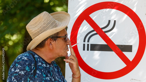 Konstfotografi Man smokes cigarette near prohibition sign