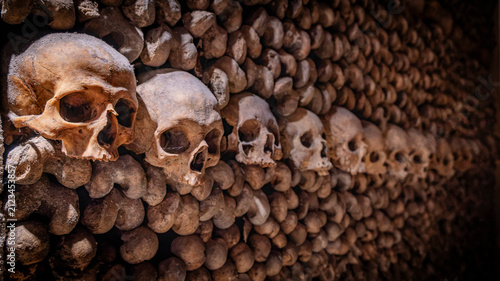 Cuadro en lienzo Row of human skulls lining a wall of stacked bones and receding into darkness in