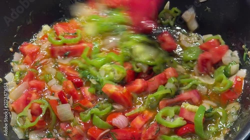 Close-up of fresh colorful vegetables being sauteed in a hot pan, featuring diced potatoes, carrots, green peppers, and red chili peppers being stirred with a spatula. Perfect for cooking tutorials, h
