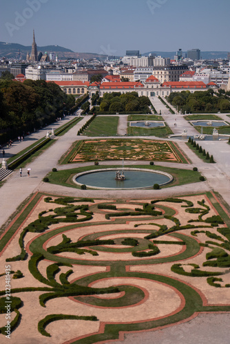 Veduta aerea e panoramica dei giardini barocchi del Palazzo del Belvedere con fontana e geometrici ricami di siepi, con lo sfondo del Belvedere Inferiore e lo skyline della città di Vienna, Austria.