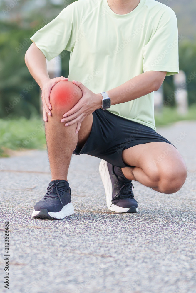 Fototapeta premium Young adult male runner with knee pain from ACL injury or patellofemoral syndrome. Man having joint ache, ligament tear or patellar tendinitis during running. Sports medical and healthcare concept