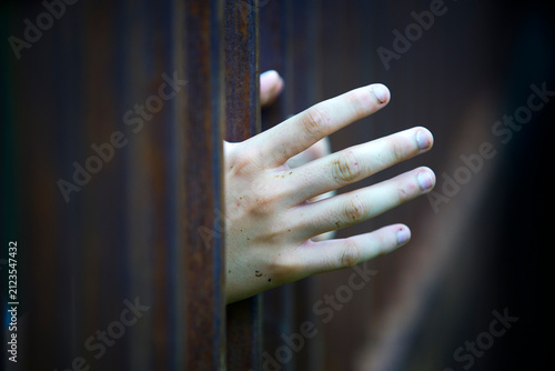 Child Hand Reaching Through Vertical Rusty Metal Bars with Focused Detail