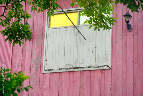 Weathered closed wooden window on faded pink wooden house exterior wall