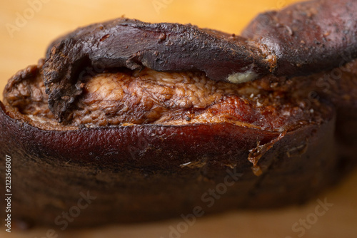 Bild auf Leinwand Close-up of a compact piece of smoked pork with darkly seared skin and spiced meat on a warm wooden surface with a shallow depth of field