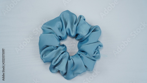Minimal flat lay of a light blue satin scrunchie on a white wooden background. Trendy hair accessory with soft texture for fashion and beauty stock photography.