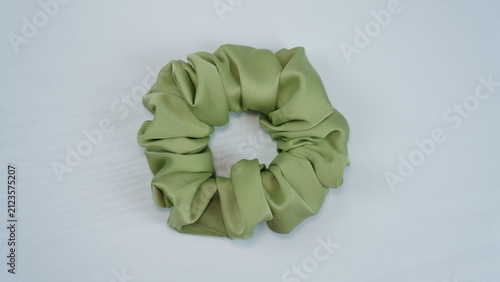 Sage green satin scrunchie placed on a white wooden table. Minimal flat lay with soft lighting, elegant hair accessory for fashion, beauty, and lifestyle concepts.