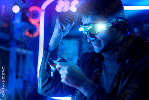 Male gamer, wearing headphones, is playing online video games or competing in esports, displaying a triumphant gesture in a neon-lit gaming room.