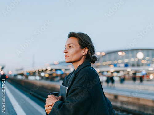 Young business Woman Standing at Train Station Platform in Blue Coat at Dusk