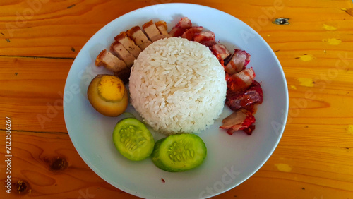 A traditional Indonesian rice dish served on a white plate, featuring steamed white rice surrounded by sliced roast pork, crispy pork belly, a boiled egg, and fresh cucumber slices.