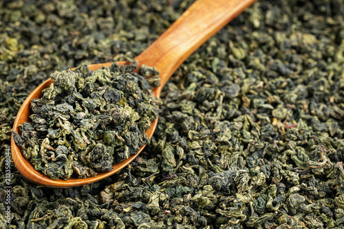 Wooden spoon filled with Tie Guan Yin leaves on neutral backdrop