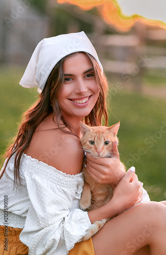 A young woman is holding a ginger kitten outdoors.