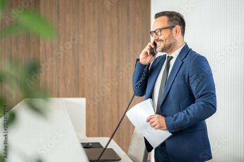 Businessman making a phone call, holding documents, creating a professional scene representing communication, work, and corporate activity in a modern office environment