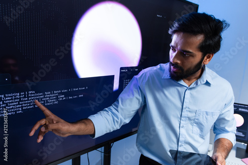 Indian Male Engineer Pointing at Monitoring Dashboard While Discussing Technical Results. Indian Male Developer Discussing Coding Strategy and Machine Learning Model with Team.
