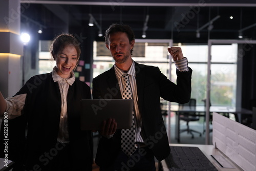 Fotografía Open mouthed cheering seizes the pair once more as they toast their success over the laptop, alone among the silent desks and dark partitions of the midnight office