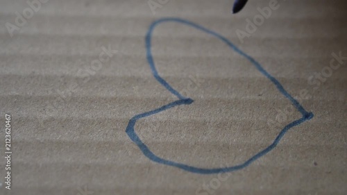 Hand drawing a heart with a blue highlighter on cardboard, representing love, warmth, or simple emotional expression, close-up