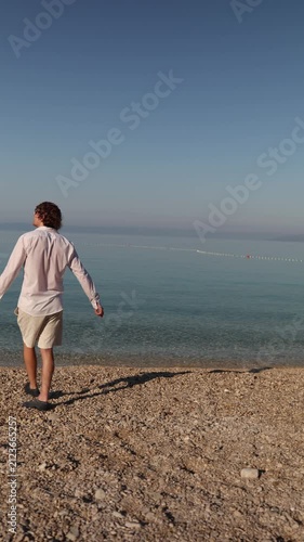 Vertical screen A carefree traveler stretches out his arms while walking beside the calm sea embracing the joy of vacation freedom and a peaceful Mediterranean morning