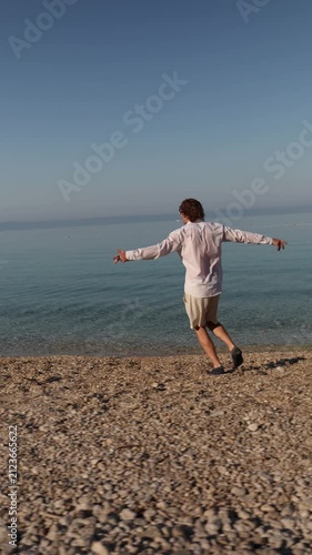 Vertical screen Vacation at last A carefree man walks along a quiet pebble beach enjoying freedom sunshine and the peaceful rhythm of the sea after busy working days