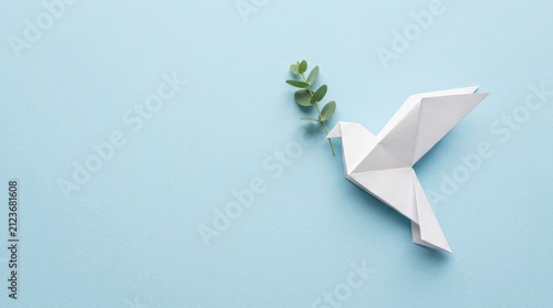 Elegant white origami dove carrying a green olive branch on a soft blue background symbolizes global peace and hope, perfect for international day of peace and spiritual concepts and