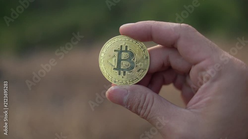Hand holding a gold Bitcoin coin against a lush green forest background, illustrating cryptocurrency, blockchain technology, and modern investment.