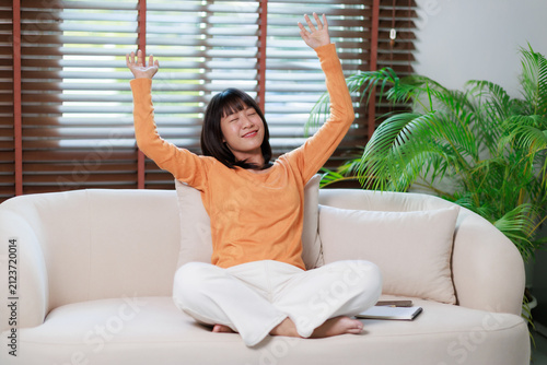 фотографія Young asian woman stretching arms up, relaxing and unwinding on a comfortable so