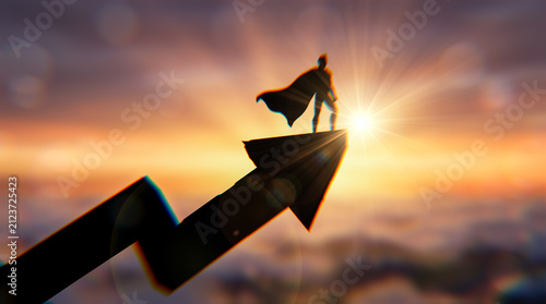 Powerful male superhero silhouette wearing cape standing confidently atop sharp rising financial arrow high above fluffy clouds during vibrant golden sunset background