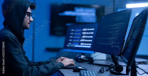 Hacker male wearing hoodie typing on computer keyboard in dark room, Concept of cybersecurity, cybercrime, software engineering, dark web, data breaches and modern digital network protection