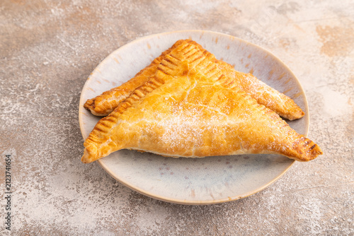 Triangles Pie, Puff Pastry, Samsa with cherry jam on brown concrete, side view, close up