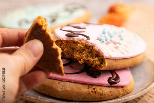 Glazed pink and blue decorated cookies with hand on brown concrete, close up, side view, selective focus