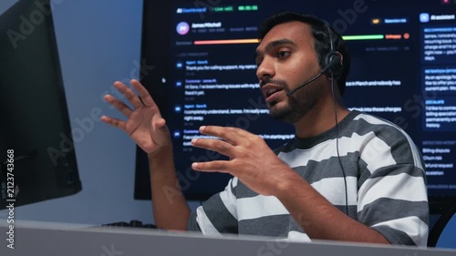 Male IT Support Specialist Providing Online Live Support, Assistance to Customer, Analyzing Technical Problem and Explaining Solution Through Headset Communication Using Desktop Computer at desk.