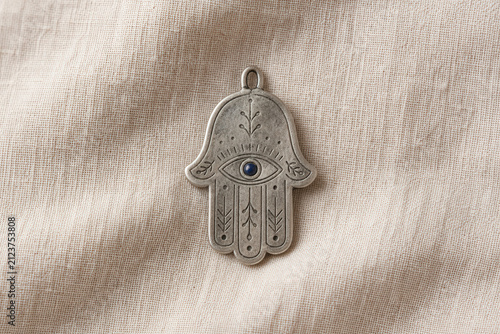 Silver Hamsa Hand Amulet with Blue Evil Eye on Linen Fabric