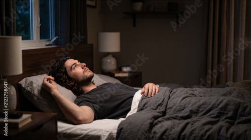 Young man lying awake and staring at the ceiling during a sleepless night. Insomnia and racing thoughts concept
