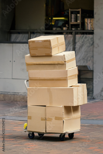 stack of sealed cardboard shipping boxes loaded on hand truck outside commercial building, ready for delivery or pickup, logistics, courier services,, warehousing, transportation, package distribution