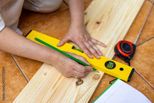 Hands use yellow level and pencil to mark wood board. Concept of precision measurement essential to quality diy carpentry work.