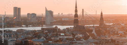 Panoramic aerial photograph of the unmistakable skyline of Riga Old Town with the spires of St Peters Church and the Dome Cathedral rising above the red-tiled roofs, at sunset. Riga, Latvia.