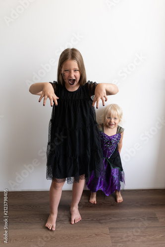 Girl in witch costume growling with younger sister in background on white studio background